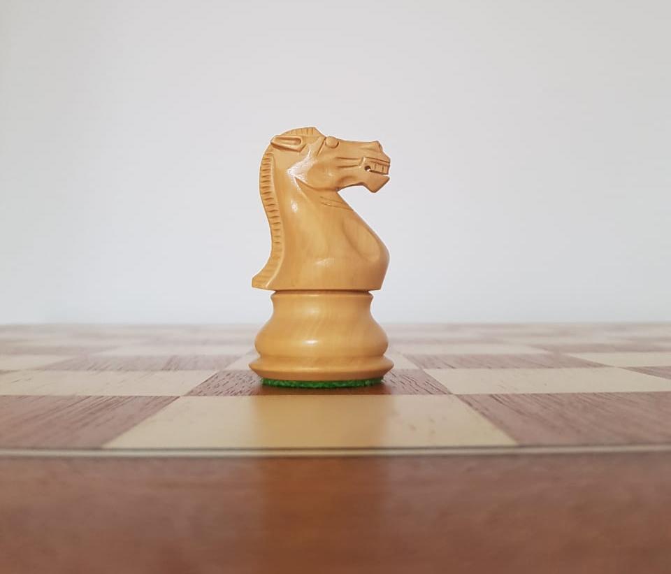 Caballo de ajedrez de madera, del bando blanco, sobre un tablero de ajedrez, también de madera.
